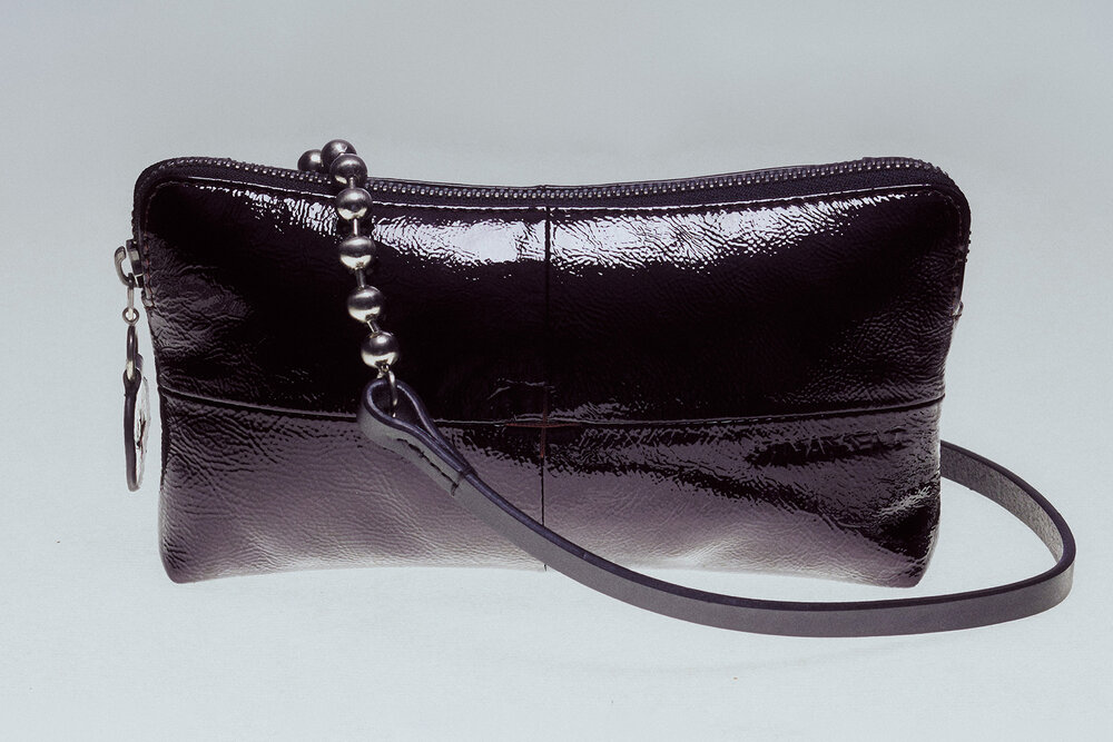 A black, glossy leather INA KENT wristlet purse with a zip closure, beaded zipper pull, and detachable leather strap, displayed against a plain background.