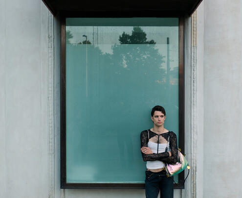 A person stands in front of a large window with a red awning labeled "WALTZ," holding INA KENT items and looking at the camera.