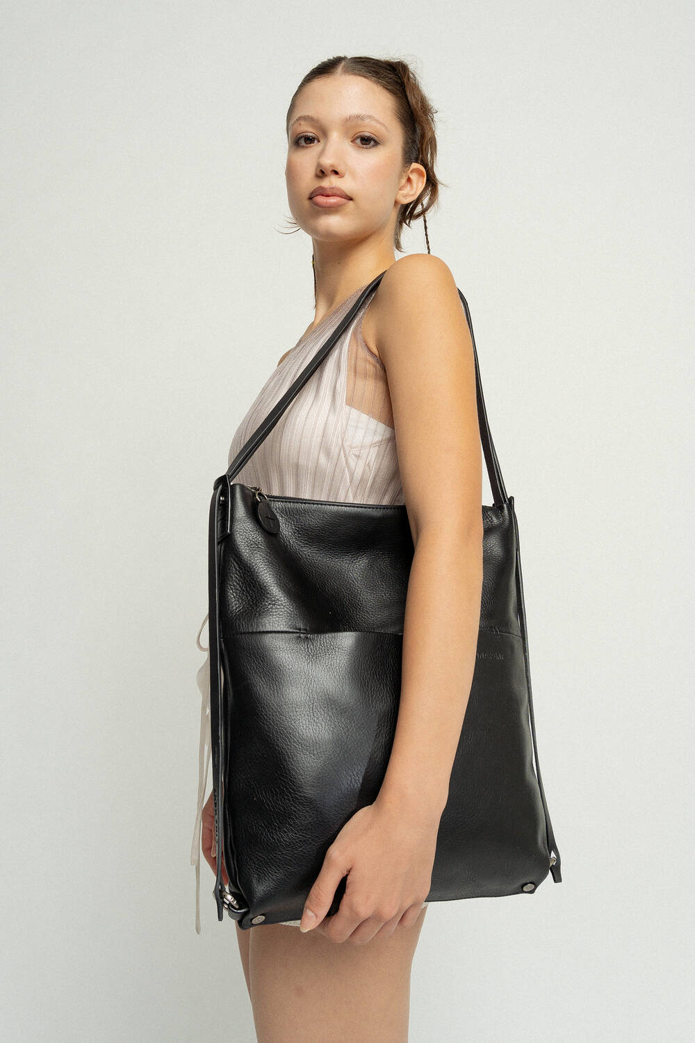 Eine Person in einem hellen ärmellosen Oberteil hält eine große schwarze INA KENT-Ledertasche auf der Schulter und blickt geradeaus. Der Hintergrund ist schlicht und weiß.