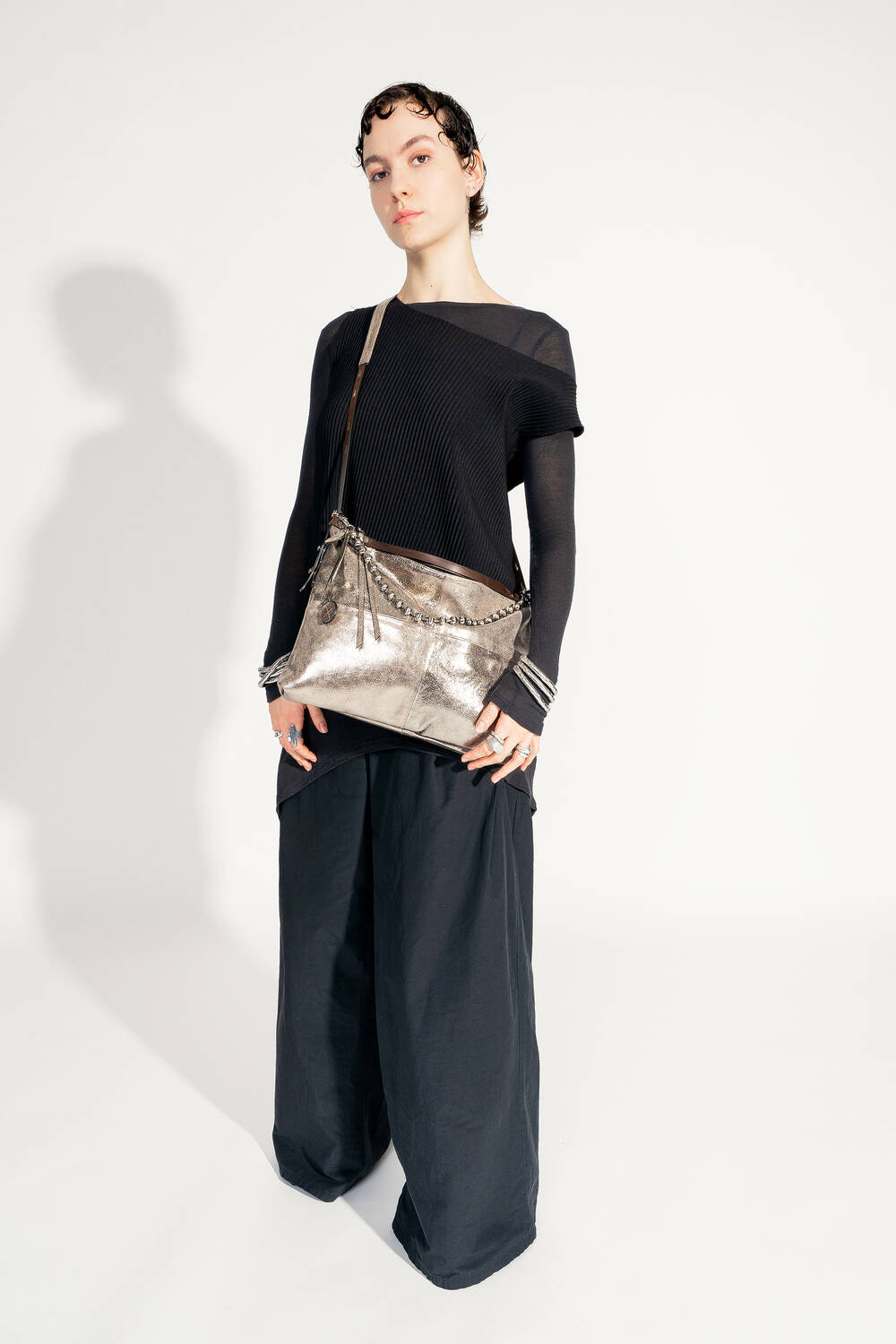 Model with INA KENT ROVE ed.3 metallic bright anthra (slanted, worn from the side): The bag is worn over the shoulder and shows off its clear shape and shimmering surface. The model is wearing an elegant black outfit.