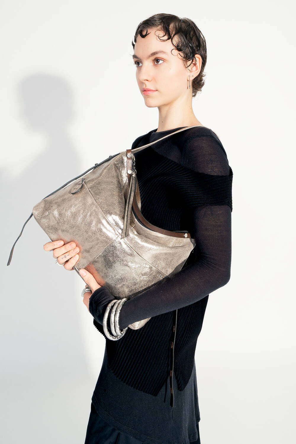 Model with INA KENT ROVE ed.3 metallic bright anthra (in hand, front view): The model holds the bag in front of her with both hands, emphasizing the shiny metallic anthracite surface and the practical size. The bag looks modern and versatile.