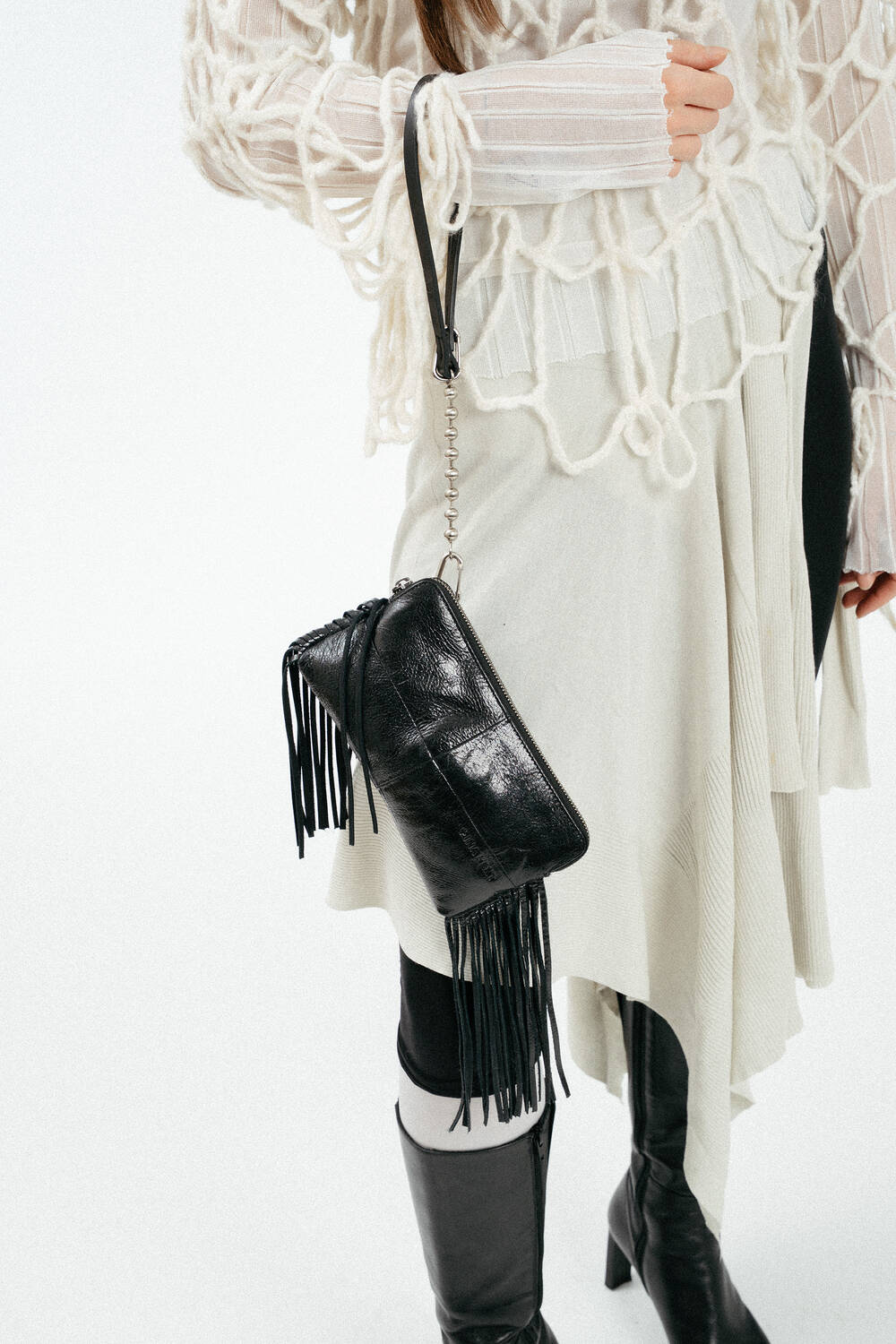 An Handgelenk baumelnde schwarze, glänzende Ledertasche mit Fransen