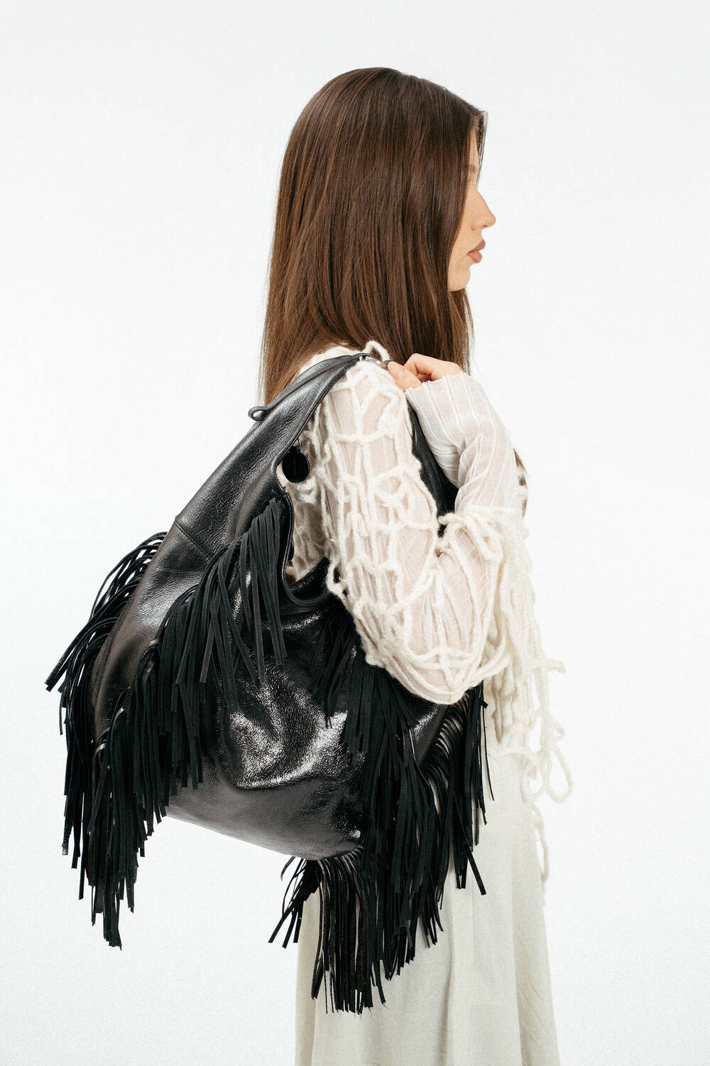 Weiblich gelesenes Model mit schwarzer Ledertasche mit Fransen auf der Schulter