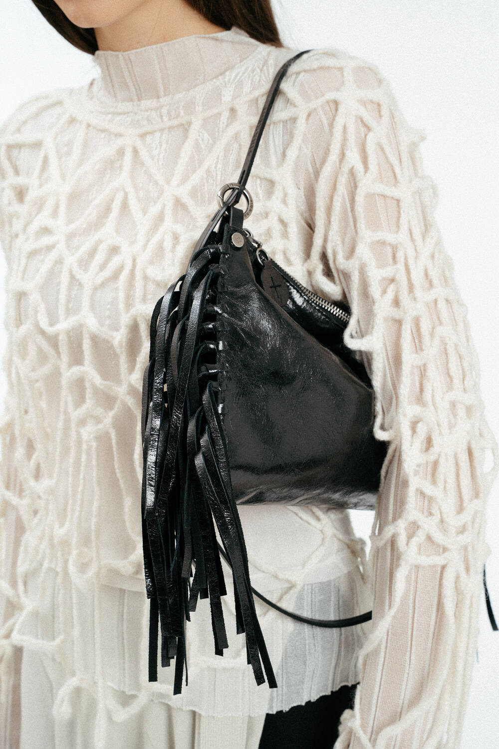 Weiblich gelesenes Model in losem, weißen Strick, mit schwarzer Ledertasche mit Fransen auf der Schulter