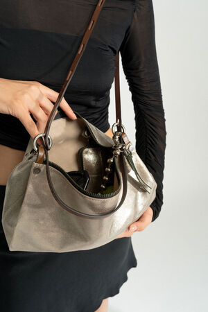A person wearing a black top and skirt is holding an open INA KENT silver handbag, revealing a cell phone and other contents inside.