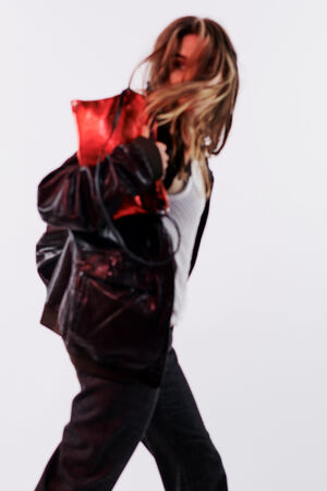 Person wearing a stylish black jacket and holding a chic INA KENT red bag, striding with dynamic motion against a plain white background.