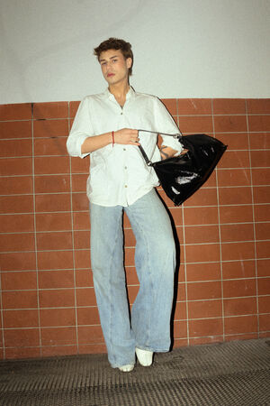 A male figure is wearing a white shirt and blue jeans. He is holding the “DINKUM ed.2” bag in patent black.