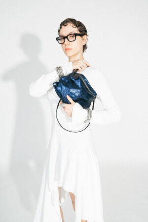 Close-up of the MOONLIT ed.1 in Crackled Deep Navy, held in the wearer's hand. The texture of the bag becomes more visible and emphasizes the metallic surface. It is carried by a black, narrow strap.