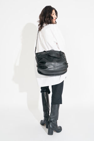 Person in a white shirt and black pants, carrying a large INA KENT leather bag. They are wearing black knee-high boots and facing sideways.