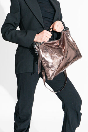 Person in a black suit elegantly holds a large, shiny bronze INA KENT handbag against a pristine white background.