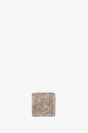 A small, rectangular, textured metal tag with a hole at the top center, featuring subtle INA KENT branding, placed against a plain white background.