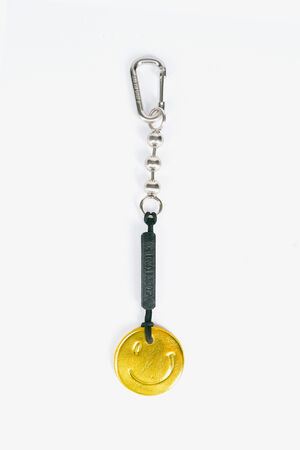 Ein Schlüsselanhänger mit silbernem Karabiner, schwarzem Verbinder und goldfarbenem runden Anhänger mit Smiley auf weißem Grund – ein auffälliger Akzent für Ihre Tasche von INA KENT.