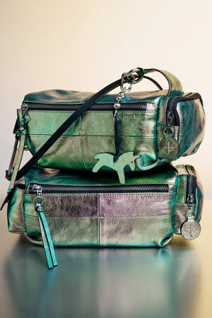 Zwei metallic-grüne INA KENT Handtaschen mit Reißverschlüssen und münzförmigen Schlüsselanhängern sind vor einem neutralen Hintergrund übereinander gestapelt.