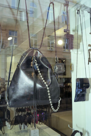 Eine schwarze Lederhandtasche mit Kettenriemen von INA KENT wird neben mehreren kleineren Accessoires und Geldbörsen in einem Schaufenster ausgestellt.