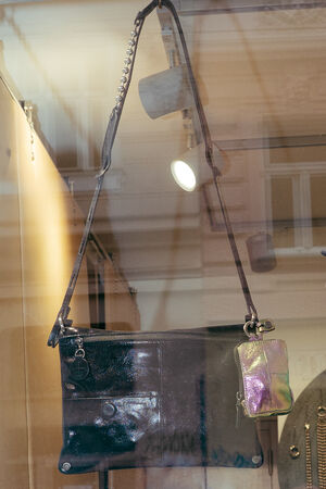 Eine schwarze Lackleder-Umhängetasche von INA KENT mit einem Kettenriemen und einem kleinen schillernden Beutel, ausgestellt in einem Schaufenster.
