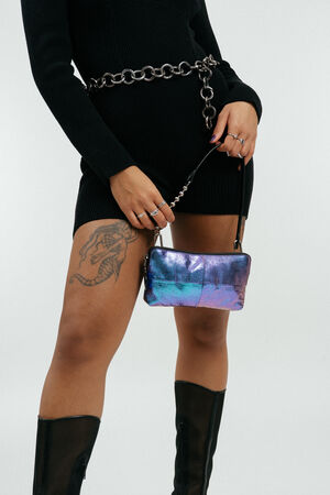 Person wearing a black dress, chain belt, and black boots holds an iridescent INA KENT purse; a snake tattoo is visible on their thigh.