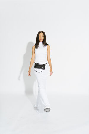 A person wearing a long white dress and an INA KENT black waist bag stands against a plain white background.