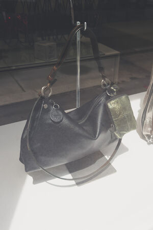 Eine schwarze Lederhandtasche von INA KENT mit einer grünen Metalltasche wird auf einem Metallständer in einem Schaufenster ausgestellt.