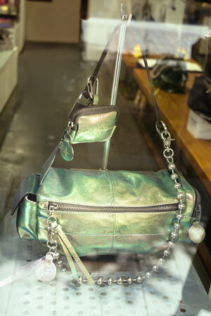 In einem Schaufenster wird eine metallisch grüne Handtasche von INA KENT mit Perlenriemen und passendem Münzbeutel ausgestellt.
