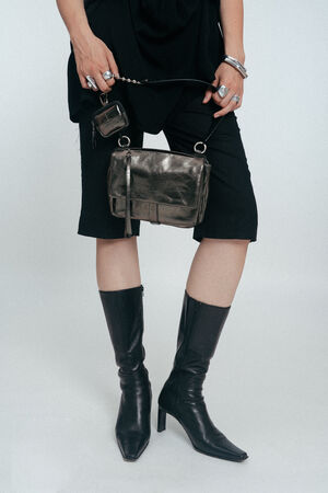 Person wearing black knee-length shorts, black pointed-toe boots, and holding an INA KENT metallic handbag and keychain; only lower half of body is visible.