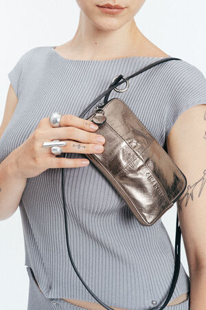 A person wearing a light gray ribbed top holds a small metallic silver INA KENT crossbody bag and wears silver rings on their fingers.