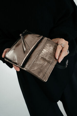 A person dressed in black holds open a metallic, zippered INA KENT wallet, displaying card slots and a compartment.