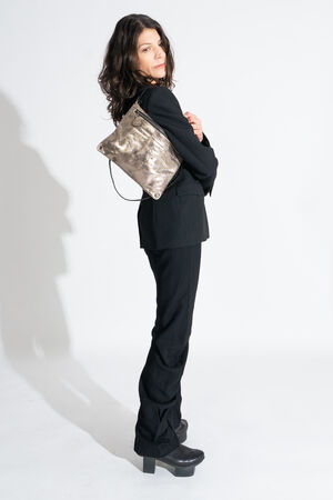 A person stands in profile wearing a black suit and platform shoes, carrying an INA KENT metallic shoulder bag against a plain white background.