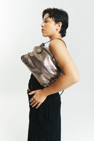 Eine schwarz gekleidete Person posiert im Profil und hält eine INA KENT Metallhandtasche unter dem Arm vor einem schlichten weißen Hintergrund.