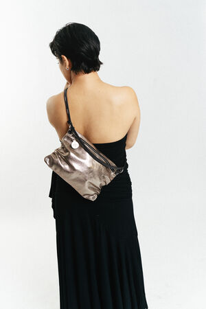 Eine Frau mit kurzen dunklen Haaren, die ein schwarzes, schulterfreies Kleid trägt, steht mit dem Gesicht nach hinten und trägt eine metallene INA KENT-Umhängetasche.