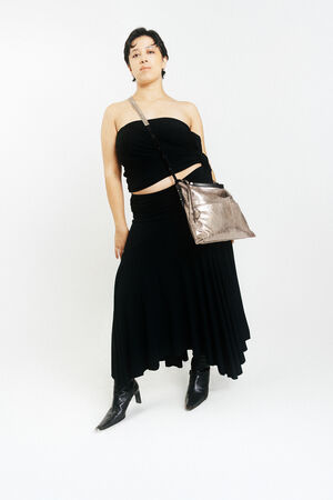 Person wearing a black strapless top, black asymmetrical skirt, black boots, and an INA KENT metallic crossbody bag stands against a plain white background.