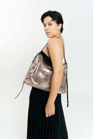 Person wearing a black top and skirt, posing sideways with an INA KENT metallic shoulder bag against a plain white background.