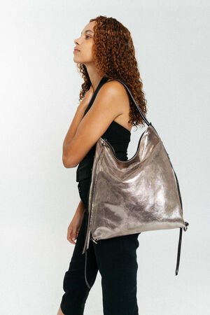 Eine Frau mit lockigem Haar und schwarzem Outfit trägt eine große, metallisch silberne INA KENT-Umhängetasche vor einem schlichten, hellen Hintergrund.