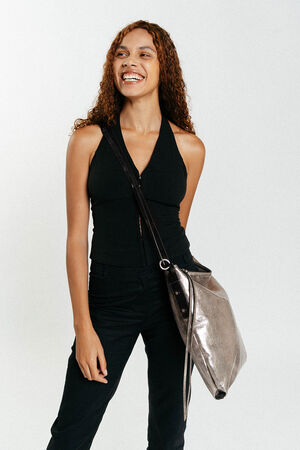 Eine Frau mit lockigem Haar, die ein ärmelloses schwarzes Oberteil und eine schwarze Hose trägt, steht lächelnd da und trägt eine große silberne INA KENT-Umhängetasche.