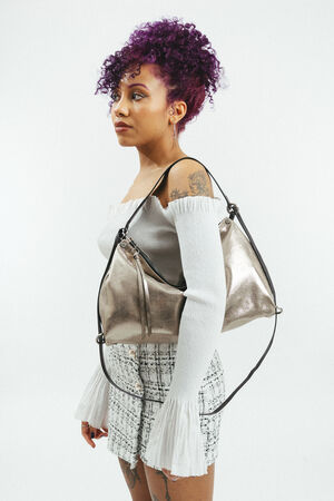 Weiblich gelesene Person mit goldener Tasche mit schwarzem Riemen am Rücken