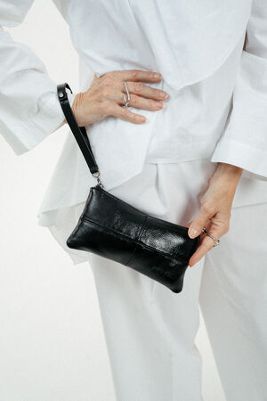 Weiß gekleidete Person, die eine kleine schwarze Lederhandtasche von INA KENT an der Hüfte trägt.