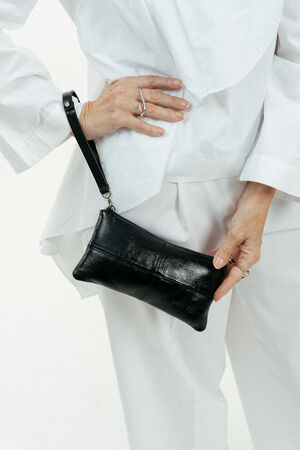Eine weiß gekleidete Person hält eine schwarze Lederhandtasche von INA KENT an ihrer Hüfte.