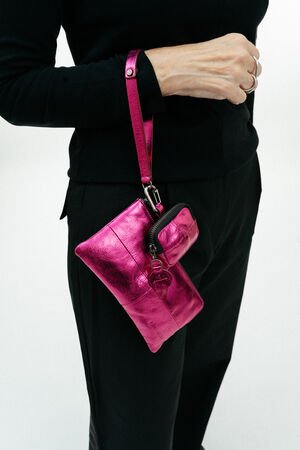 A person wearing black holds an INA KENT metallic pink wristlet bag with a matching small pouch attached.
