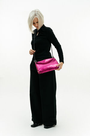A woman with gray hair wearing black clothing stands while holding a bright pink INA KENT shoulder bag against a plain white background.