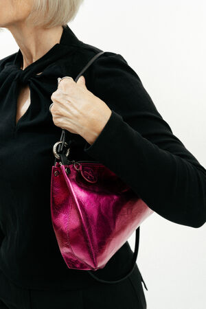 A person with short blonde hair, wearing a black top, holds an INA KENT shiny metallic pink handbag with a black strap over their shoulder.