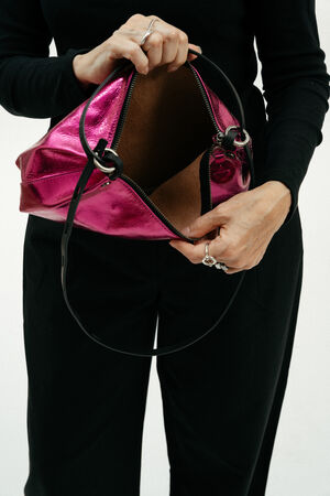 A person in black clothing holds open a metallic pink INA KENT handbag, showing the empty interior against a plain white background.