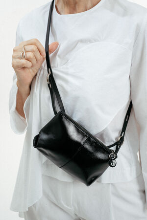 Person wearing a white outfit with an INA KENT black leather crossbody bag and a silver ring on their left hand, shown from the shoulders to the waist.