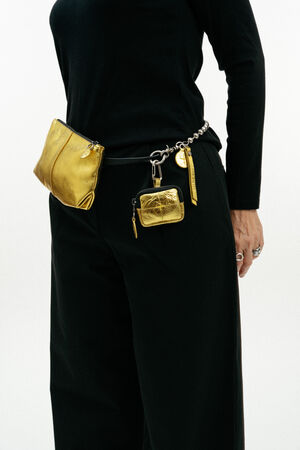 A person wearing black clothes with an INA KENT gold pouch and small gold accessory attached to a black belt at their waist.