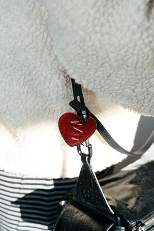 kleiner, roter Anhänger in Herzform aus Leder an schwarzer Ledertasche