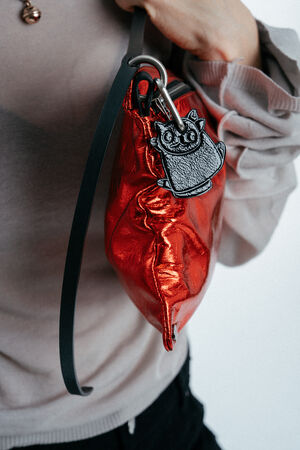 A person holds a shiny red INA KENT handbag with a black strap and an attached cat-shaped keychain.