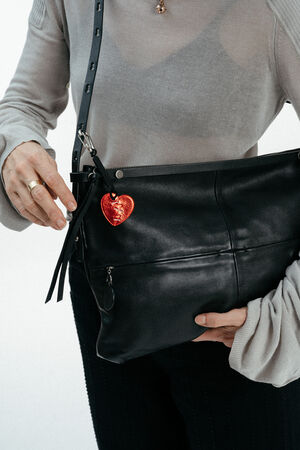 A person wearing a gray top holds an INA KENT black leather handbag with a red heart-shaped keychain attached to it.