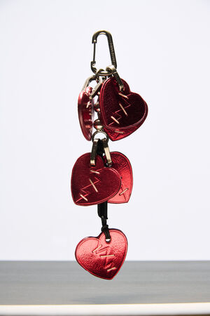 A set of metallic red heart-shaped keychains with stitched designs by INA KENT hangs from a black carabiner against a plain background.