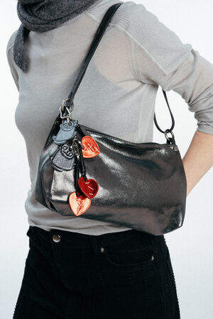 Person wearing a sheer grey top and black pants, carrying an INA KENT shiny black shoulder bag decorated with metallic red and silver heart-shaped keychains.