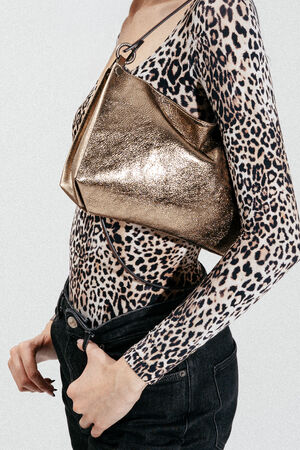 Person wearing a leopard print long-sleeve top and black jeans, holding an INA KENT metallic gold handbag under their arm against a plain background.