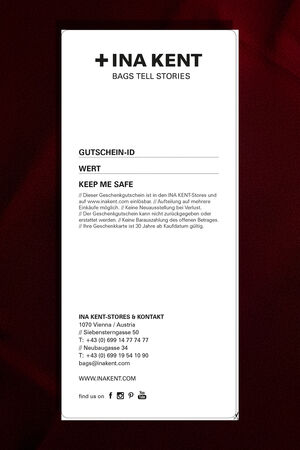 A rectangular INA KENT gift card features the brand’s store details, terms, and contact information printed in black on a crisp white background.