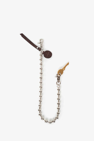 A beaded silver keychain from INA KENT with a brown leather tag, a round brown charm, and a brass key attached, displayed on a white background.
